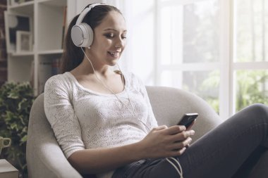 Mutlu genç kadın evde, müzik o onun smartphone ile bağlanma ve giyen kulaklık