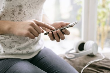 Pencere kenarında oturan ve evde, onun smartphone ile bağlanma kadın eller yukarı yakın