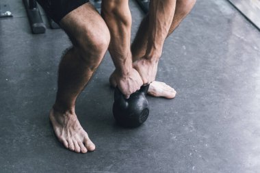 Spor salonunda egzersiz yapan atletik bir adam halter olarak ağırlık kaldırıyor.