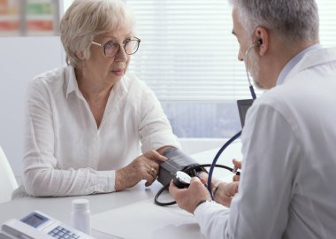 Üst düzey bir kadın hastanın tansiyonunu, hipertansiyonu ve önleme konseptini ölçen profesyonel bir doktor.