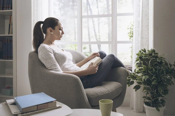 Pen Ung Kvinne Som Slapper Hjemme Sitter Ved Vinduet Leser – stockfoto