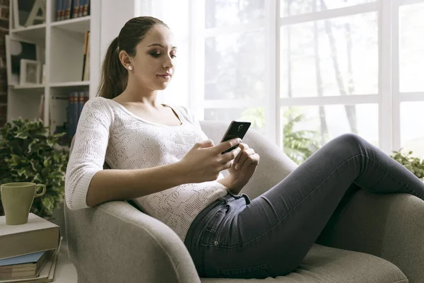 Mujer Joven Relajándose Sillón Casa Conectándose Con Teléfono Inteligente Ella —  Fotos de Stock