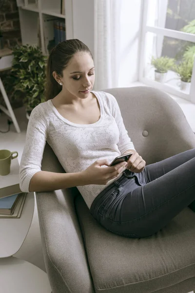 Mujer Joven Relajándose Sillón Casa Conectándose Con Teléfono Inteligente Ella — Foto de Stock