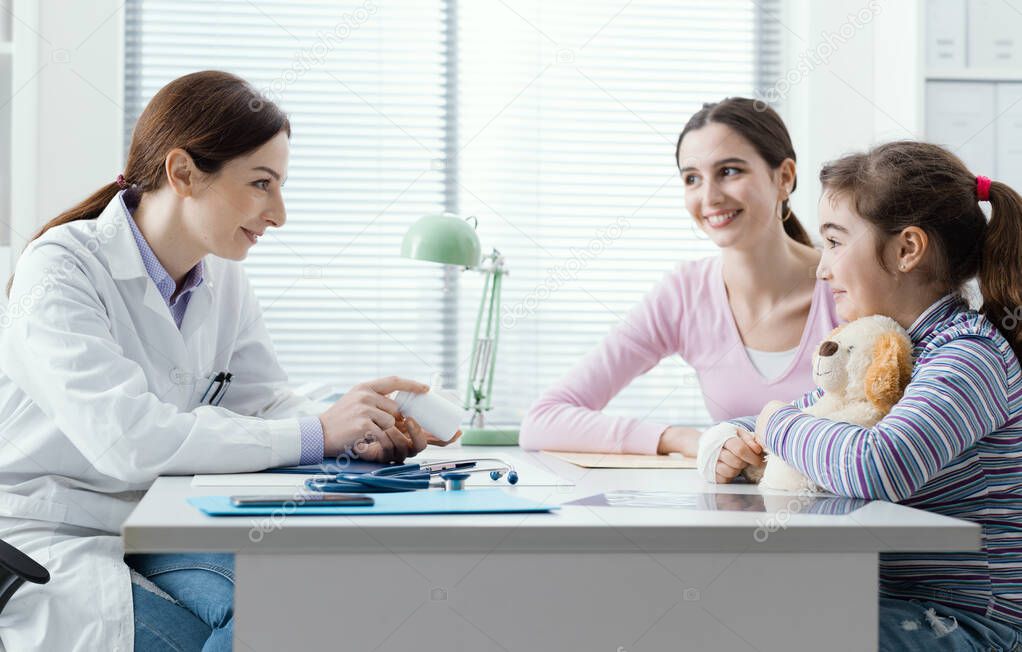 Professional pediatrician giving a prescription medicine to a young girl, she is showing a bottle of pills