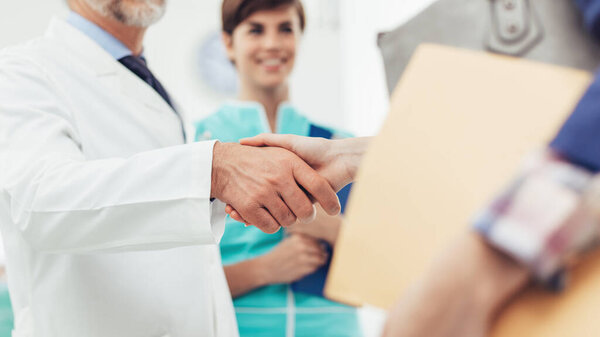 Medical staff welcoming a patient at the clinic: the doctor is giving an handshake and smiling, medical service and healthcare professionals concept, hands close up