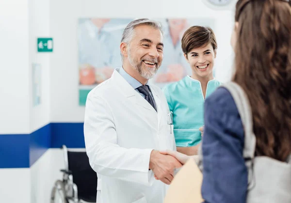专业的微笑医生在诊所迎接一位年轻的女病人 他们正在握手 — 图库照片