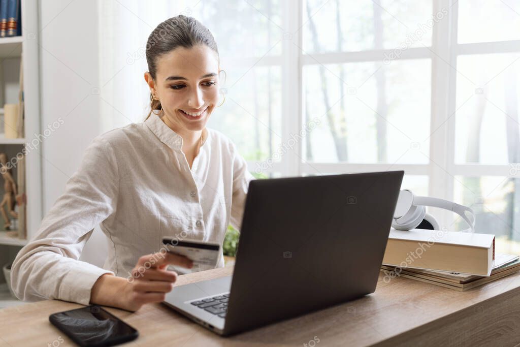 Smiling woman relaxing at home and doing online shopping on her laptop using a credit card