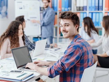 Üniversite öğrencilerinin bir araya geldiği ve birlikte çalıştığı bir grup öğrenci, ön planda bir dizüstü bilgisayarla çalışıyor