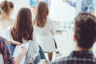 İş semineri ve sunumu, bir adam konuşma yapıyor ve seyirci dinliyor ve notlar yazıyor.