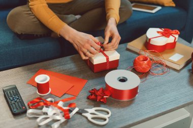 Evdeki kanepede oturan ve Noel, tatil ve kutlama konsepti için güzel hediyeler hazırlayan genç bir kadın.