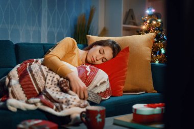 Genç bir kadın Noel arifesinde kanepede uzanıp uyuyakalıyor. Elinde uzaktan kumanda var.