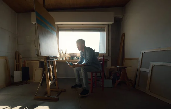 彼のスタジオに座って絵を描く創造的な若いアーティスト 彼は座っている ブラシと塗料と瓶を保持します — ストック写真