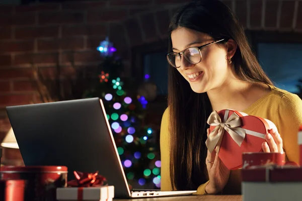年轻的微笑的女人坐在家里的办公桌前 手里拿着心形的礼品盒 假期和庆祝活动的概念 — 图库照片