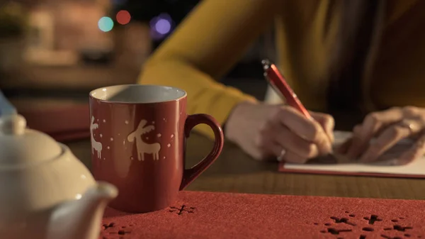 自宅の机に座ってクリスマスカードに願い事を書いている女性 休日やお祝いの概念 — ストック写真