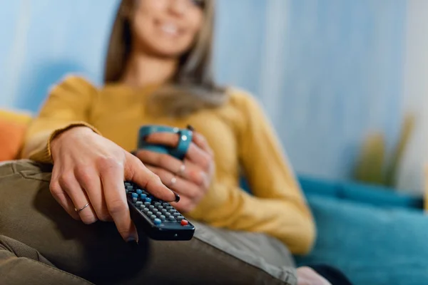 笑顔の女性は家でソファに座ってテレビを見ている彼女はリモコンを持っていると彼女の好きなテレビ番組を見て — ストック写真