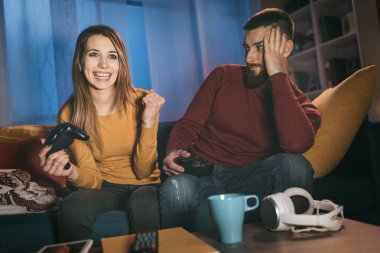 Evde video oyunu oynayan mutlu çift, kız kazandı ve yumruğunu kaldırarak kutluyor.