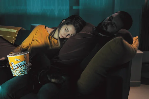 Young sleepy couple sitting on the couch and falling asleep while watching a movie