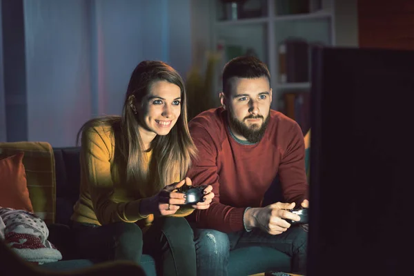 Happy couple playing video games together at home, they are sitting on the sofa and holding a game controller, entertainment and lifestyle concept