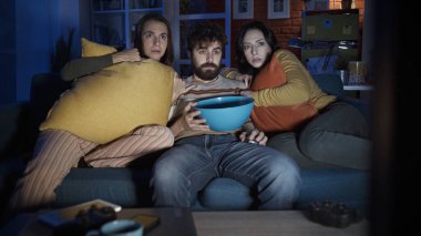 Friends sitting on the sofa at home and watching scary horror movie together, entertainment concept clipart