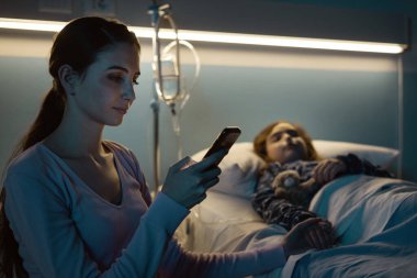 Geceleri çocuğuna hastanede yardım eden genç bir kadın akıllı telefonuyla sohbet ediyor ve internete bağlanıyor.