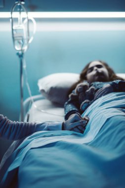 Hasta çocuğuna yardım eden bir kadın gece hastanede yatarken elini tutuyor.