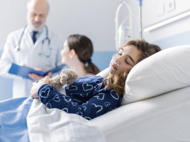 Hastanede yatakta yatan bir çocuk, yanında bir doktor ve annesi, pediatri ve sağlık konsepti var.