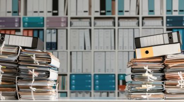 Ofiste dosya ve evrak yığınları ve arka planda kitap rafları: yönetim ve arşiv kavramı