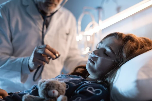 专业医生在夜间检查躺在病床上的一名儿童 他正在使用听诊器检查她的呼吸 — 图库照片
