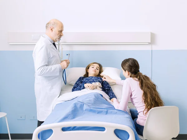 入院中の若い患者を見舞いに来た医者はベッドに寝そべっていて母親は隣に座っている — ストック写真