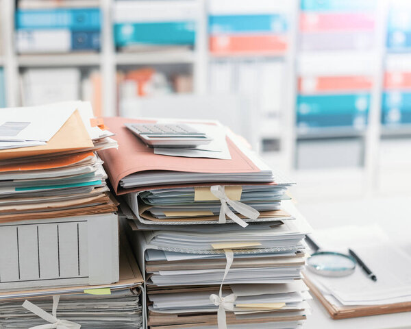 Пачки файлов и документов в офисе и книжные полки на заднем плане: концепция управления и хранения
