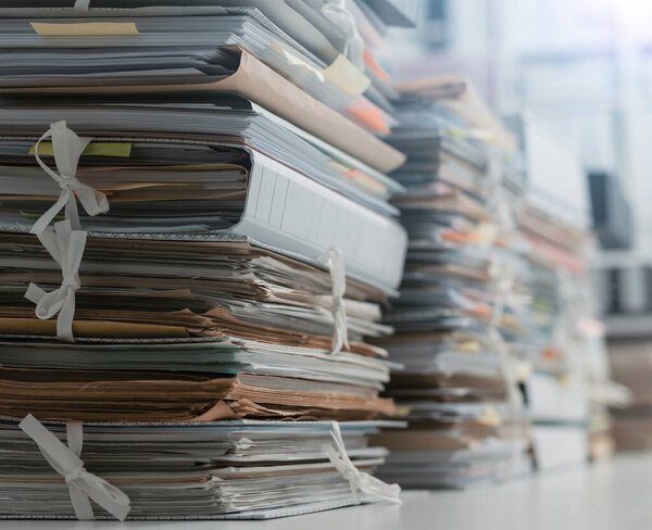 Stacks of paperwork and files in the office: work overload, files management and administration concept