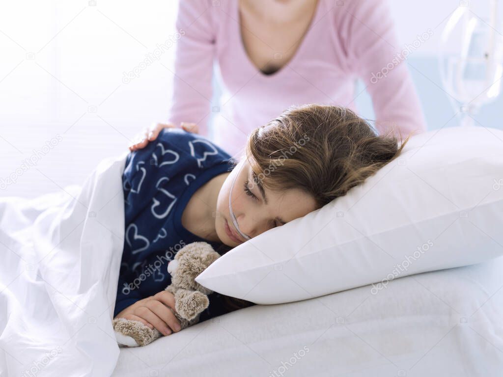Young woman assisting her sick child lying in bed at the hospital, pediatrics and healthcare concept