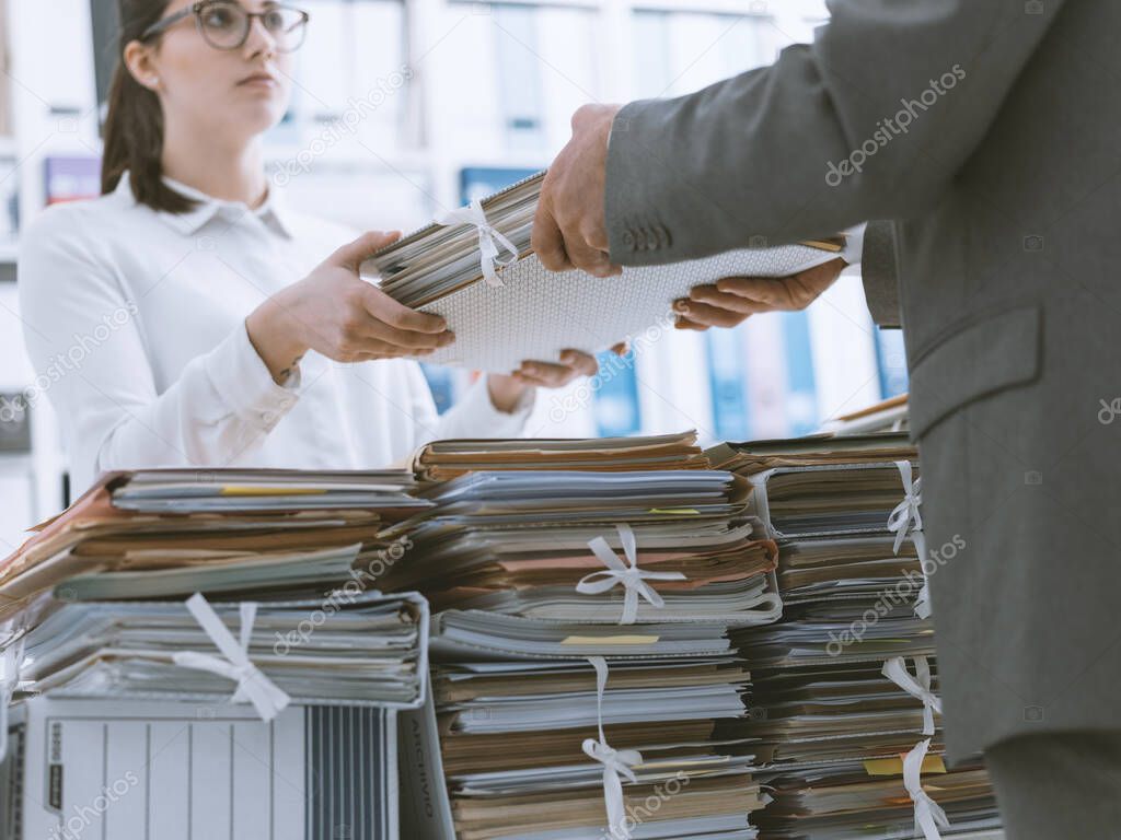Boss handing paperwork to his employee, she is overwhelmed by work