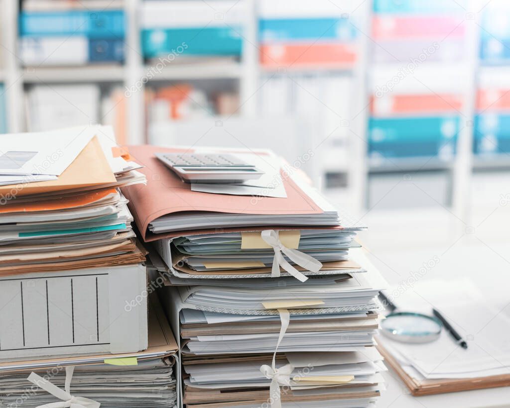 Stacks of files and paperwork in the office and bookshelves on the background: management and storage concept