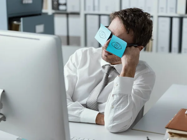 Lazy unproductive office worker wearing funny sticky notes on his glasses and hiding his closed eyes