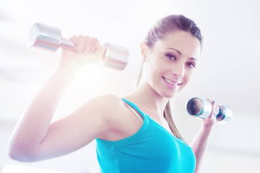 Gülümseyen ve dambıllarla egzersiz yapan çekici bir kadın..