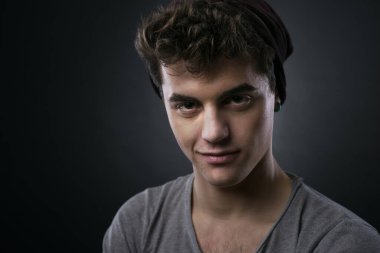 Gülümseyen yakışıklı genç adam karanlık arka planda poz veriyor.