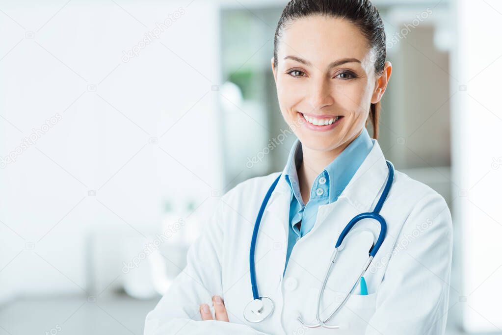 Confident female doctor posing in her office and smiling at camera, health care and prevention concept