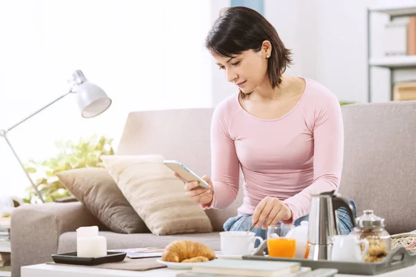 Mladá Žena Snídá Svém Obývacím Pokoji Pohovce Drží Smartphone Připojení — Stock fotografie