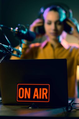 Young radio host getting ready for broadcasting, she is wearing headphones, on air sign in the foreground clipart