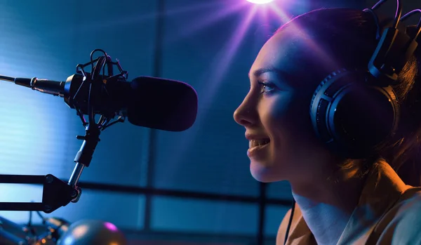 Young charming radio dj working in the studio, she is talking into the microphone, entertainment and communication concept