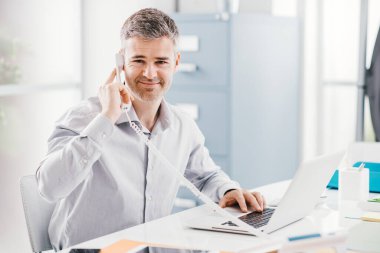 Ofisinde çalışan kendinden emin gülümseyen işadamı ve danışmanı bir telefon görüşmesi yapıyor: iletişim ve iş konsepti.