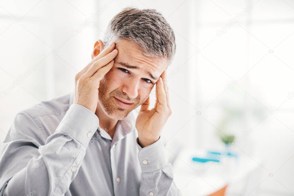 Stressed tired man having a bad headache, he is touching his temples
