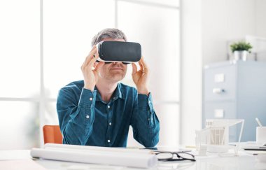 Ofis masasında çalışan profesyonel bir mimar ve VR kulaklık takıyor. Sanal gerçeklik arayüzü görüyor.