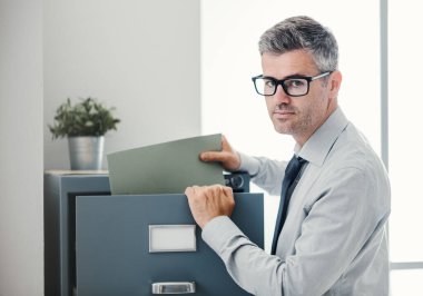 İş yerindeki iş adamı: dosya dolabındaki dosyaları araştıran profesyonel özgüvenli ofis memuru