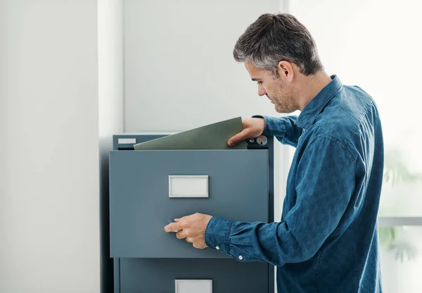 Office clerk searching files in the filing cabinet, he is looking into the file drawer