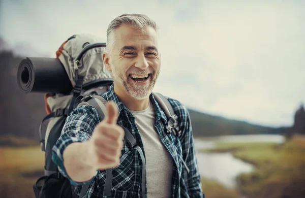 山の上で幸せな成熟したハイカーのトレッキングと親指をあげると 彼はカメラで笑っています — ストック写真