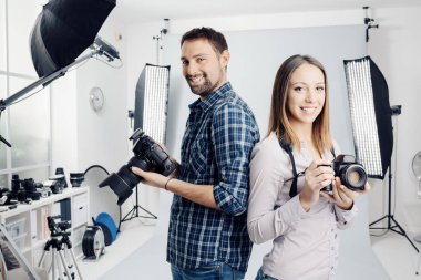 Smiling young professional photographers posing in the studio, they are holding digital cameras clipart