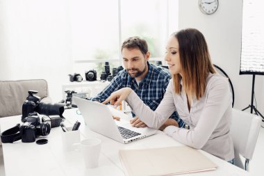 Yaratıcı bir ajansta fotoğrafçı ve tasarımcı olarak oturuyorlar ve bir dizüstü bilgisayarla birlikte çalışıyorlar.