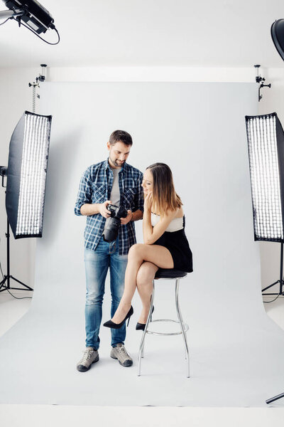 Профессиональный фотограф и молодая красивая модель позируют вместе, мужчина показывает ее фото превью на дисплее камеры

